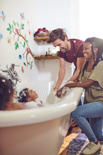 Padres juguetones dando a las hijas baño de burbujas - foto de stock