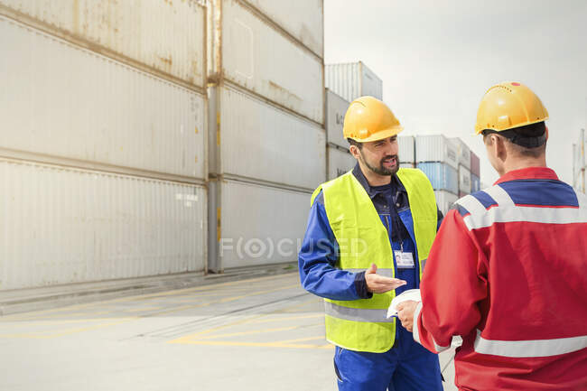 Hafenarbeiter unterhalten sich in der Nähe von Frachtcontainern auf einer sonnigen Werft — Stockfoto