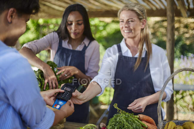 Mulher sorridente trabalhador com leitor de cartão de crédito no mercado de agricultores — Fotografia de Stock