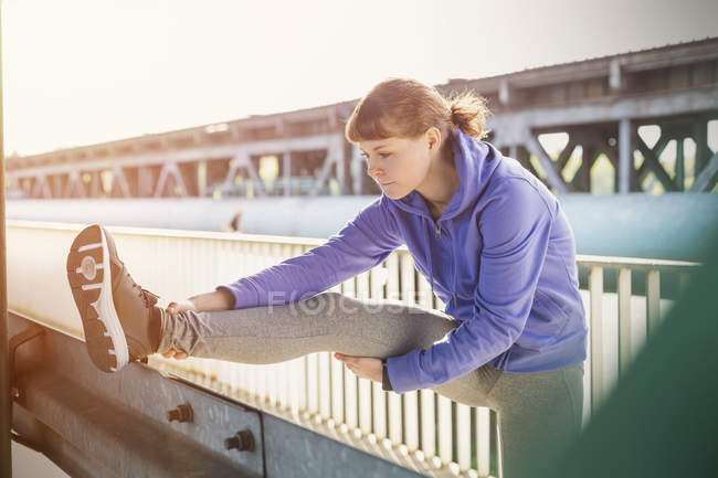 Young female runner stretching leg on urban railing — Stock Photo