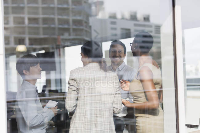 Улыбающиеся бизнесмены разговаривают в солнечном окне офиса — стоковое фото