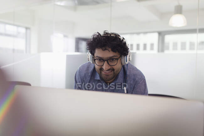 Улыбающийся бизнесмен в наушниках работает за компьютером в офисе — стоковое фото
