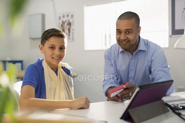 Portrait male doctor prescribing medication to boy in doctors office — Stock Photo
