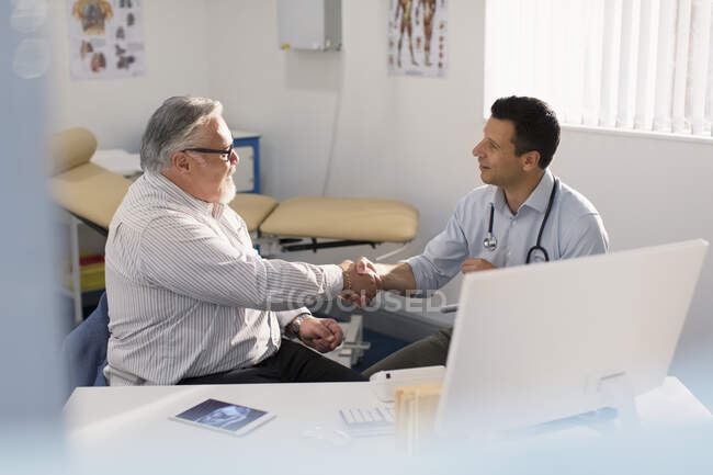 Male doctor shaking hands with senior patient in doctors office — Stock Photo