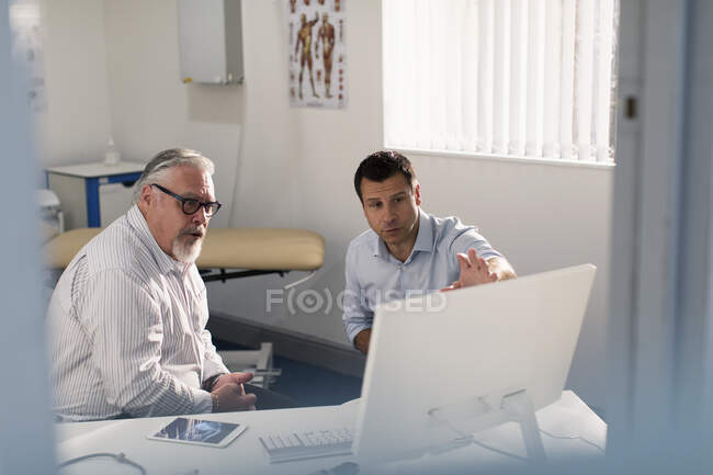 Чоловік лікар зустріч зі старшим пацієнтом за комп'ютером в офісі лікарів — стокове фото