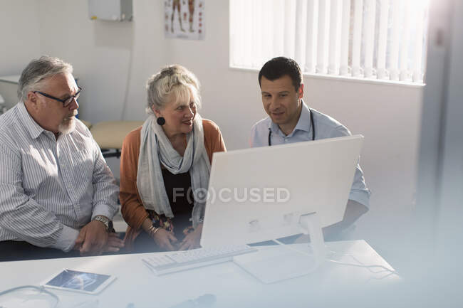 Встреча врача с пожилой парой за компьютером в кабинете врача — стоковое фото