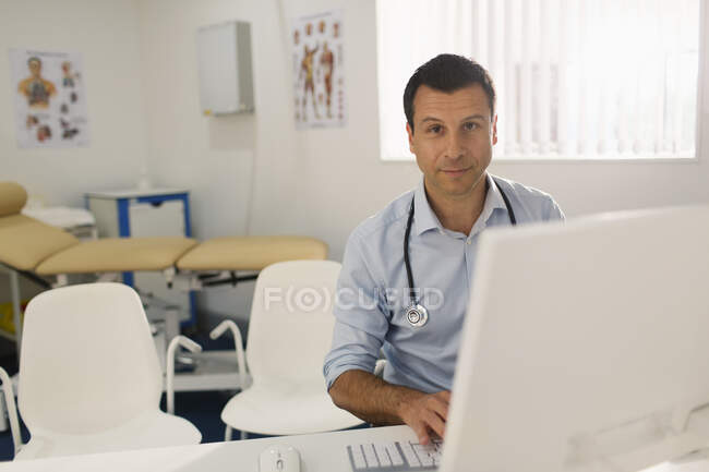 Retrato confiante médico masculino trabalhando no computador em consultório de médicos — Fotografia de Stock
