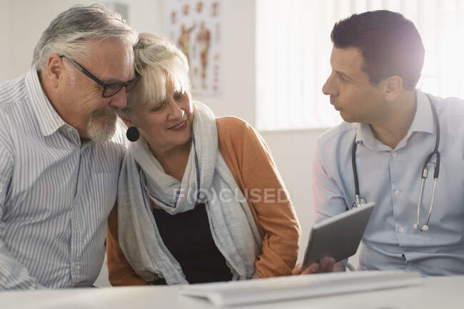 Médico masculino con tableta digital reunión con pareja mayor en el consultorio de médicos - foto de stock