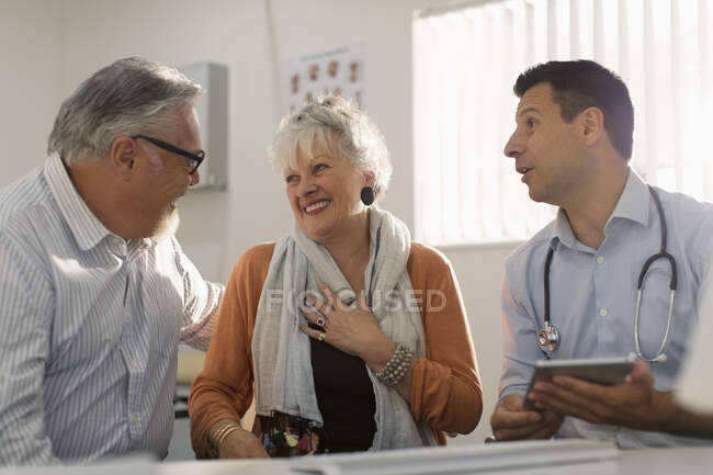 Reunión de médicos con feliz pareja de ancianos en el consultorio médico - foto de stock