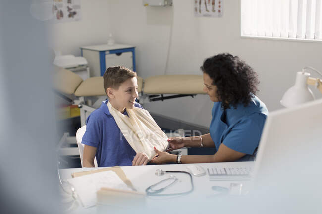 Female doctor checking arm sling of boy patient in doctors office — Stock Photo