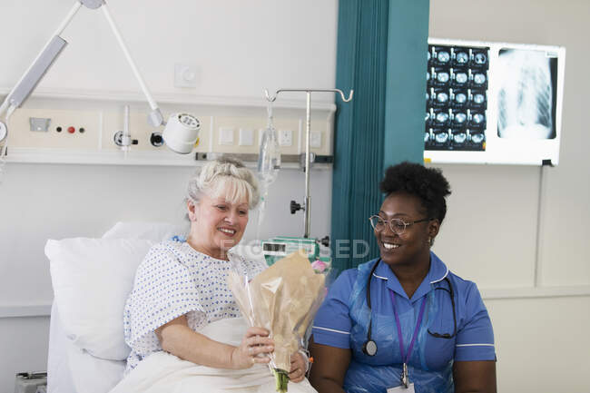 Paciente feminina mostrando flores para enfermeira no quarto do hospital — Fotografia de Stock