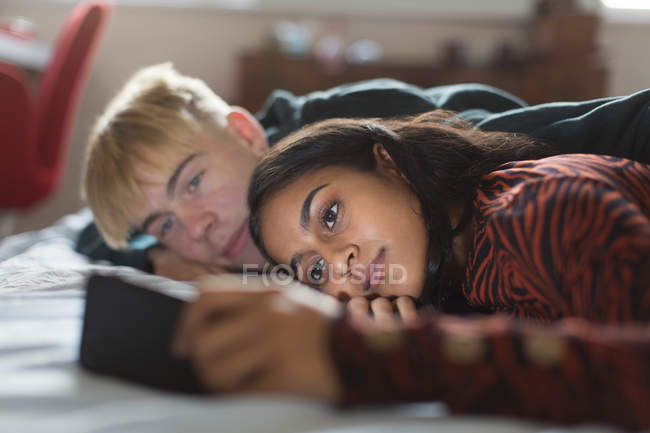 Pareja adolescente usando teléfono inteligente, acostado en la cama - foto de stock