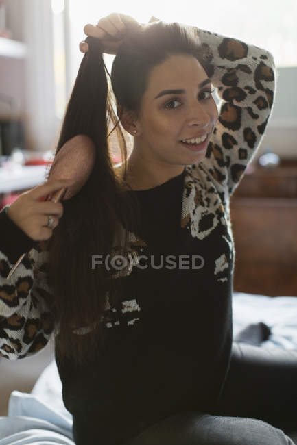 Portrait of smiling teenage girl brushing hair on bed — Stock Photo