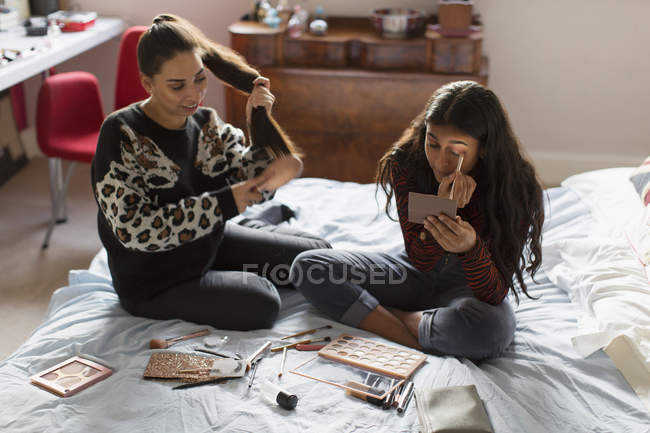Adolescentes aplicando maquillaje y cepillando el cabello en la cama - foto de stock