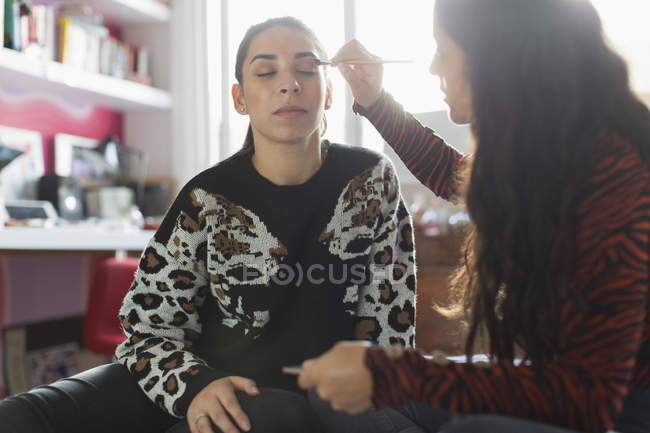 Teenage girl applying eyeshadow makeup to friends eyes — Stock Photo