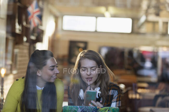 Mujeres jóvenes aplicando brillo labial en la ventana de la cafetería - foto de stock
