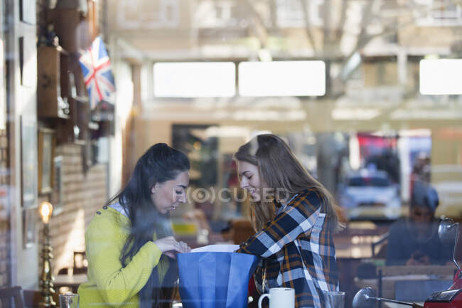 Les jeunes femmes regardant dans le sac à provisions dans la fenêtre du café — Photo de stock