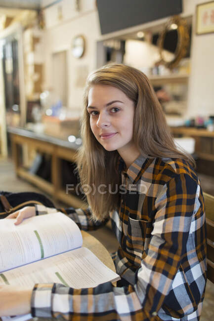 Retrato confiado joven estudiante universitaria estudiando en la cafetería - foto de stock