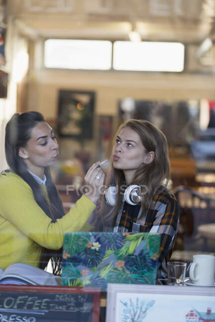Young women applying lip gloss in cafe window — Stock Photo