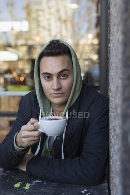 Retrato confiante jovem em cappuccino bebendo com capuz — Fotografia de Stock