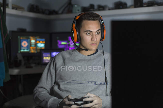 Focused teenage boy with headset playing video game at computer in dark room — Stock Photo