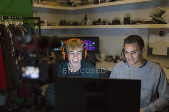 Rapazes adolescentes felizes com auscultadores a jogar jogos de vídeo no computador no quarto escuro — Fotografia de Stock