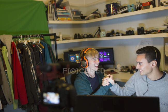 Happy teenage boys with headsets playing video game at computer in bedroom — Stock Photo