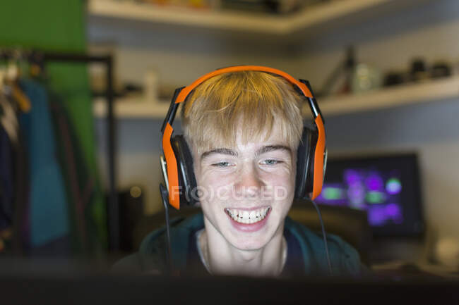 Happy teenage boy with headset playing video game at computer — Stock Photo