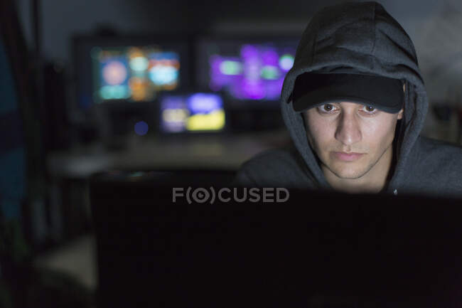 Hacker masculino com capuz usando o computador no quarto escuro — Fotografia de Stock
