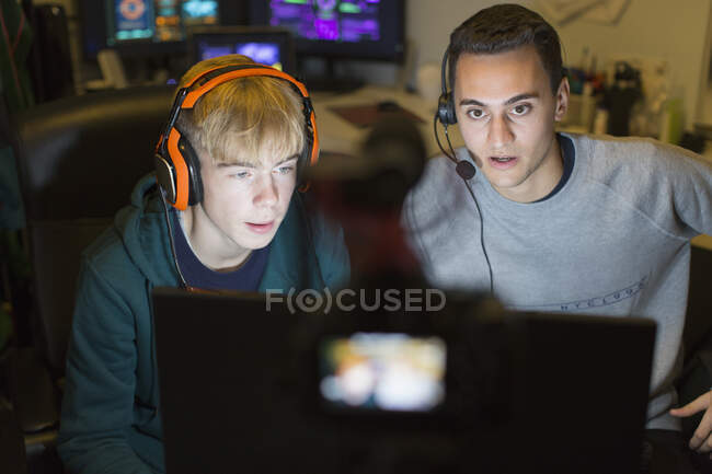 Teenage boys with headphones playing video game at computer in dark room — Stock Photo