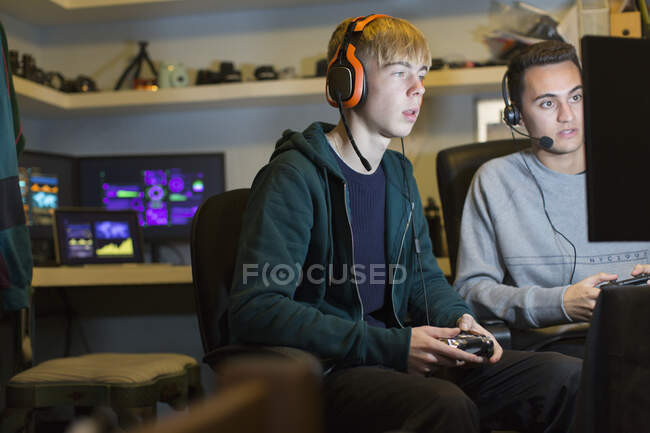 Мальчики-подростки в наушниках играют в компьютерные игры в темной комнате — стоковое фото