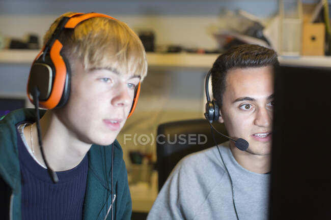 Teenage boys with headsets playing video game at computer — Stock Photo
