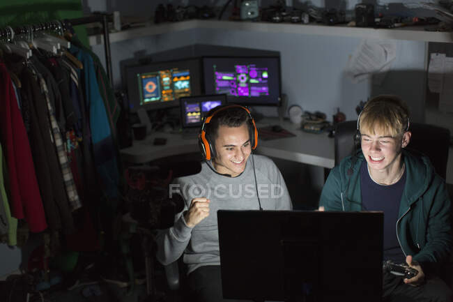 Возбужденные подростки с наушниками играют в видеоигры за компьютером в темной комнате — стоковое фото
