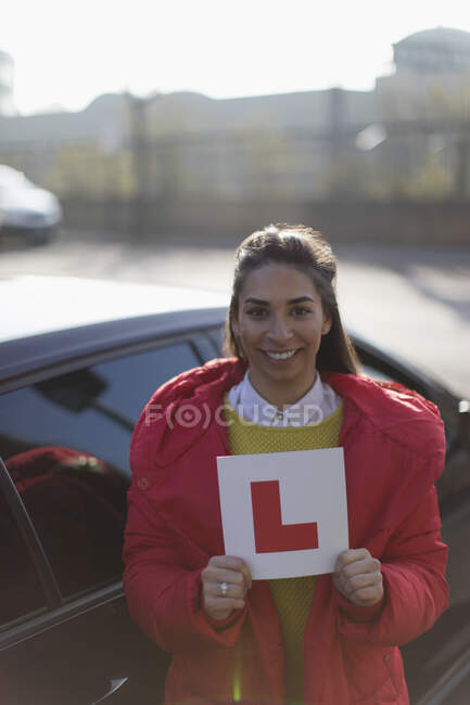Portrait happy young woman holding learner permit next to car — Stock Photo