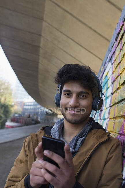 Retrato sonriente joven escuchando música con auriculares y reproductor de mp3 - foto de stock
