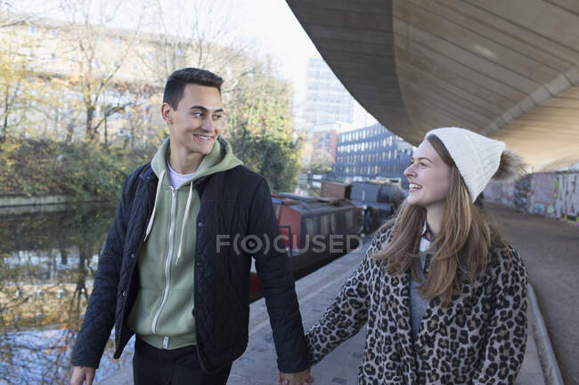 Happy young couple holding hands, walking along urban canal — Stock Photo