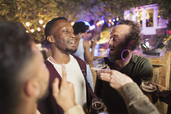 Счастливые друзья-мужчины разговаривают и пьют на вечеринке в саду — стоковое фото
