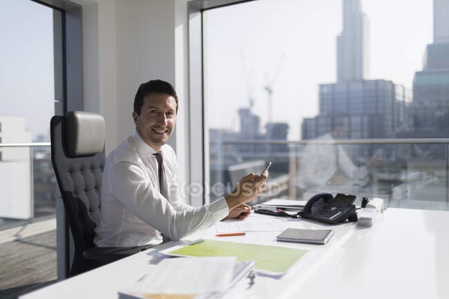 Ritratto uomo d'affari sicuro utilizzando smartphone in ufficio grattacielo — Foto stock