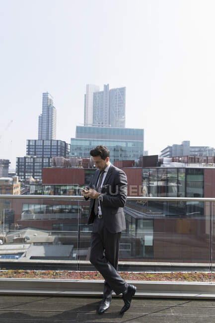 Empresário usando telefone inteligente em ensolarado, varanda highrise urbano — Fotografia de Stock