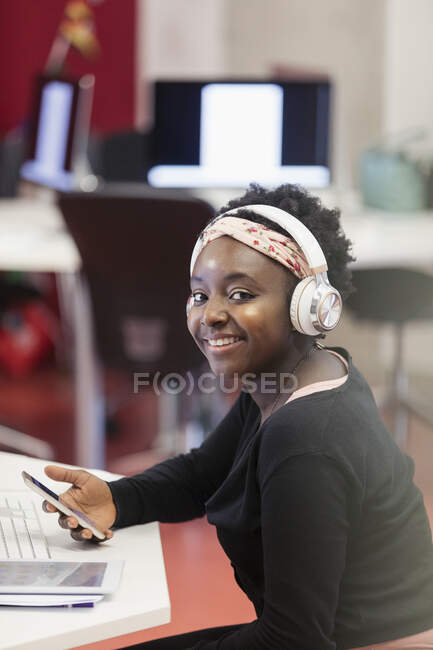 Portrait étudiante confiante avec écouteurs et téléphone intelligent — Photo de stock