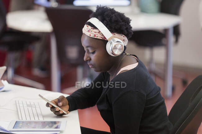 Estudante com fones de ouvido usando telefone inteligente em sala de aula — Fotografia de Stock