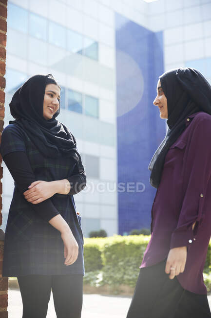 Jovens amigas em hijabs conversando fora do prédio ensolarado — Fotografia de Stock