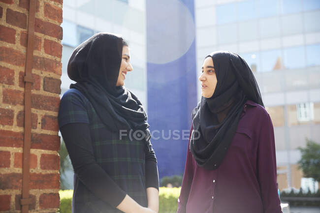 Mujeres jóvenes en hiyabs hablando fuera del soleado edificio - foto de stock