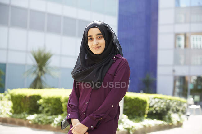 Retrato confiante jovem mulher no hijab fora edifício ensolarado — Fotografia de Stock