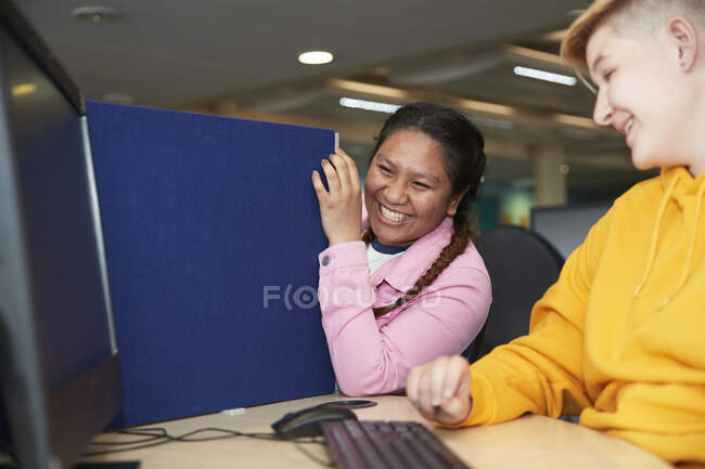 Счастливые молодые студентки колледжа смеются над компьютером в библиотеке — стоковое фото