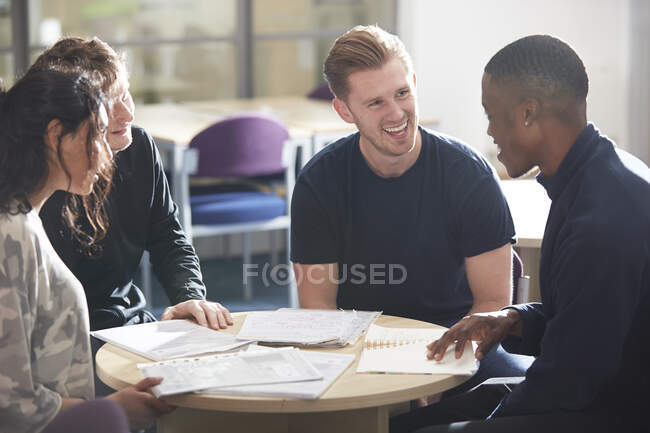 Jóvenes estudiantes universitarios felices hablando y estudiando en la biblioteca - foto de stock