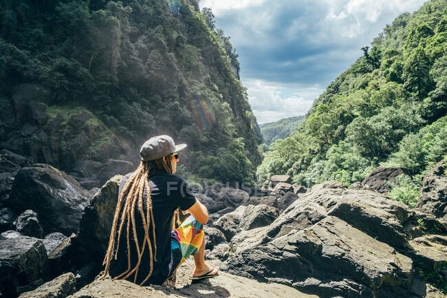 Uomo con dreadlocks seduto su rocce in boschi soleggiati — Foto stock