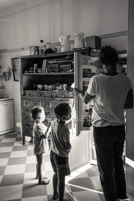 Family standing at open refrigerator in kitchen — Stock Photo