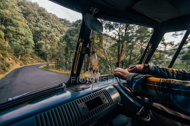 Hombre conduciendo furgoneta a lo largo de carretera remota en bosque - foto de stock