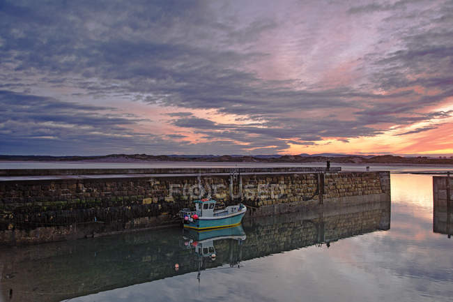 Fishing boot moored along jetty wall under dramatic sunrise sky — Stock Photo